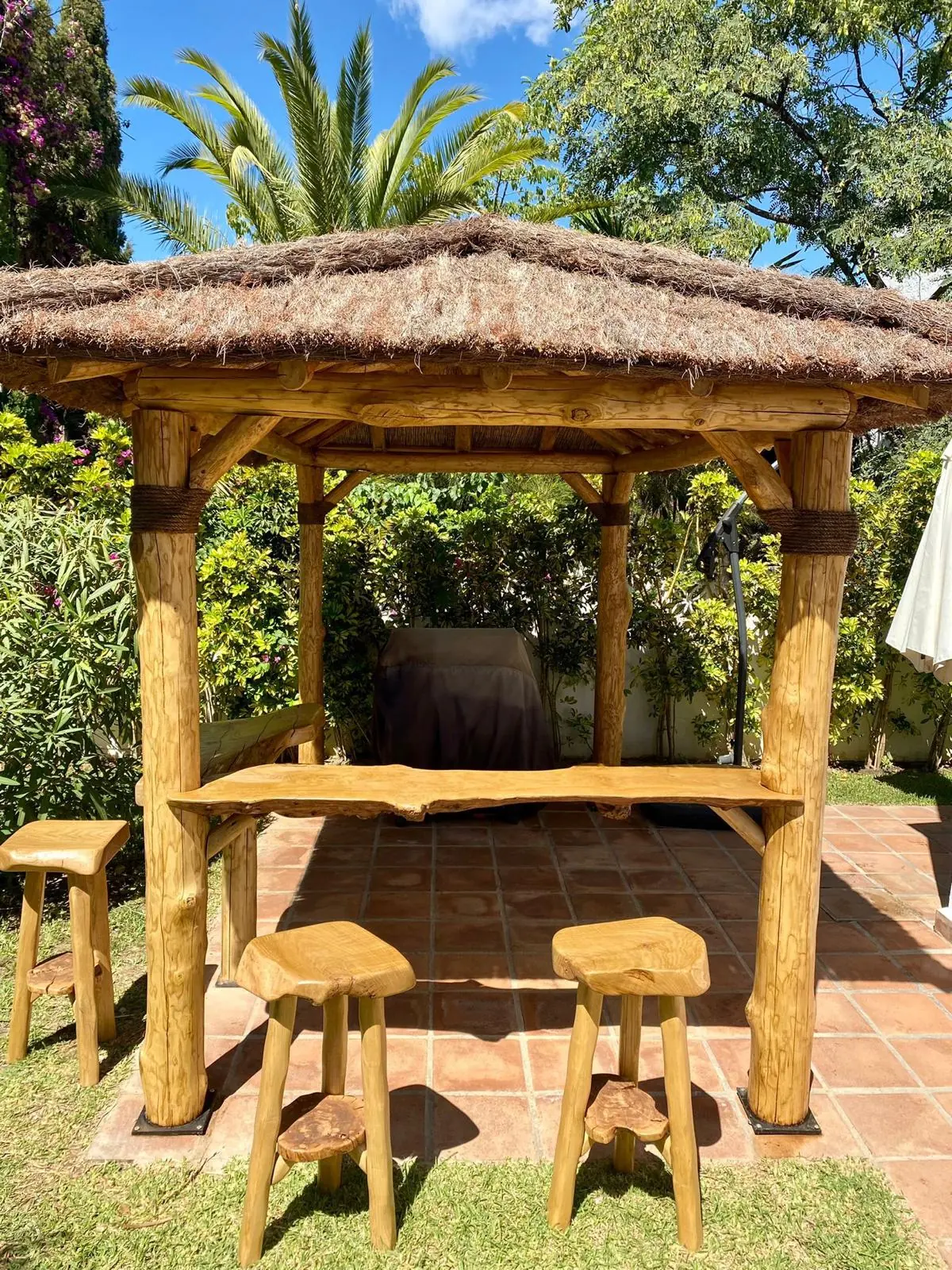 Cenador rústico de madera con cubierta de paja en un jardín de Marbella